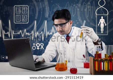 Young scientist wearing lab coat working in laboratory with laptop and chemical glassware