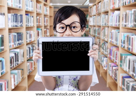 Portrait of female student standing in the library corridor while holding an empty tablet screen