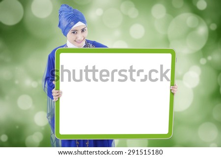 Attractive young muslim woman wearing islamic clothes and holding a blank banner, shot with defocused background