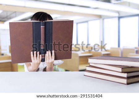 Female kindergarten school student reading textbooks in the class while covering her face