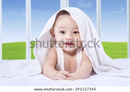 Joyful little baby boy with a cute face lying on the bed and smiling on the camera under a towel