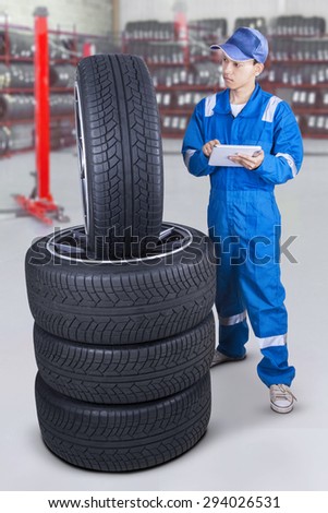 Portrait of young mechanic wearing blue uniform and using a digital tablet to check tires at workshop