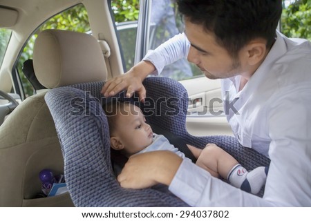Portrait of young man putting his newborn baby on the car seat