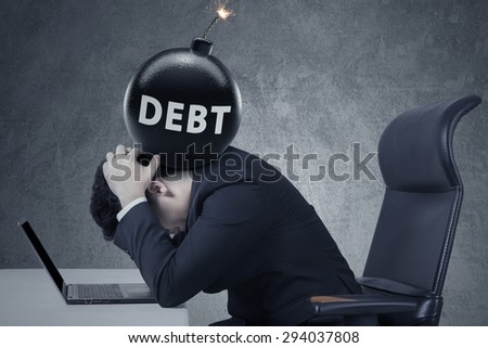Concept of business debt deadline. Stressful businessman with laptop and a bomb of debt on his head
