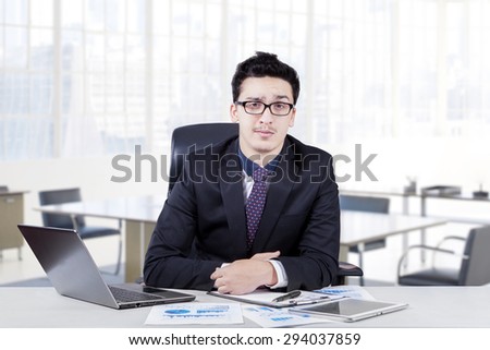 Young caucasian businessman with formal suit, sitting and smiling in the office with laptop computer and document on the table