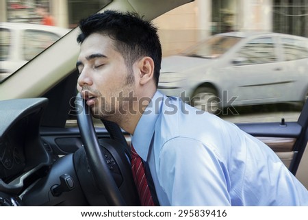 Exhausted young businessman sleeping in the car while driving the car on the road