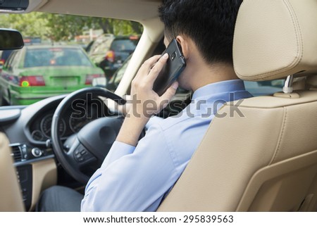 Young man driving his car on the traffic jam while speaking on the cellphone
