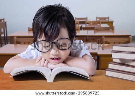 Cute girl wearing glasses and reading textbooks on the table in the classroom