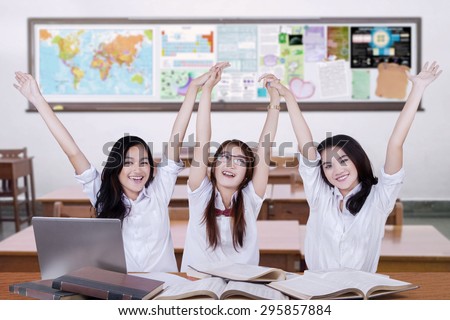 Happy high school students raise hands together while celebrating their achievement in the classroom