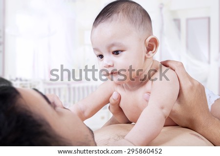 Portrait of male infant lying on the father chest while staring at the father face, shot in the bedroom
