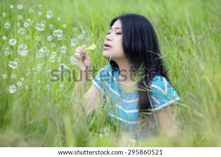 Young woman with casual clothes enjoying holiday while playing and blowing bubble at field