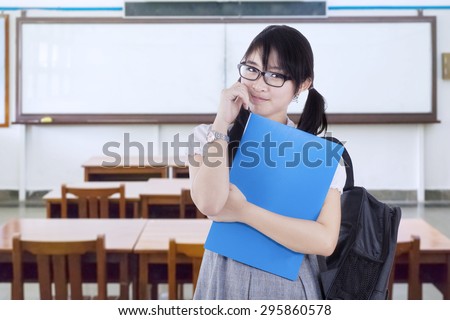 Portrait of pretty female college student holding folder while carrying backpack in the classroom