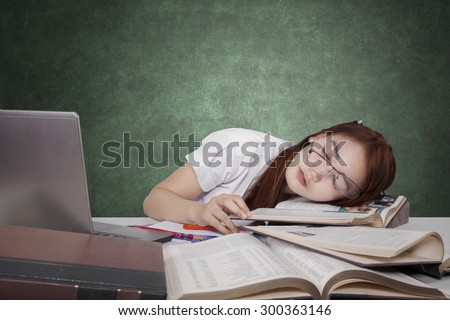 Brunette female high school student sleeping in the class above the book with laptop on the table