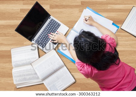 Unique perspective female student lying down on the floor while studying with laptop and books