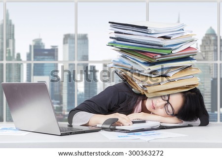 Portrait of exhausted businesswoman sleeping in the office with laptop on desk and paperwork over head