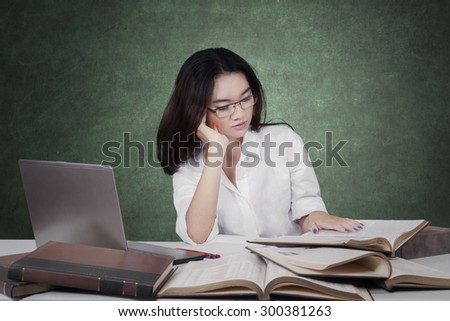 Portrait of beautiful female student with long hair, studying with laptop while reading books on desk