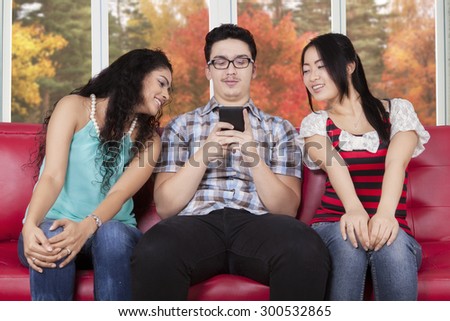 Two mixed race girls sitting on the sofa while looking at the smartphone on the guy hands
