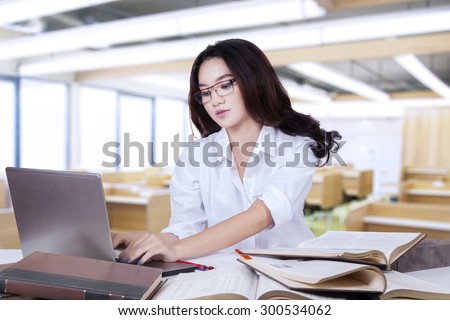 Lovely female student using laptop to study in the class with books on the table