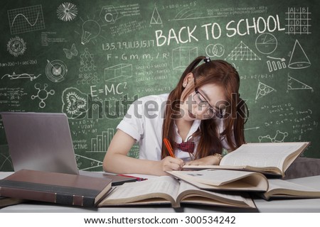 Portrait of pretty female high school student studying in the class with laptop and writing on the book