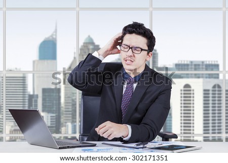 Young businessman worrying his job while scratching his head in the office