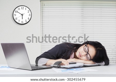 Portrait of young businesswoman sleeping on desk with laptop and paperwork in office