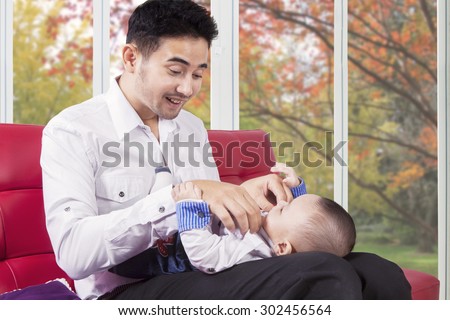 Portrait of joyful young father change his baby clothes while sitting on the sofa at home