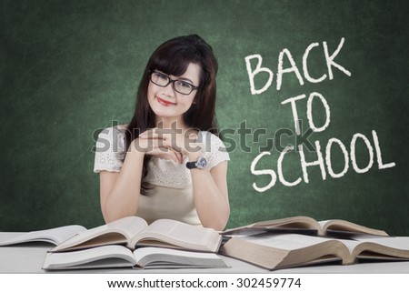 Portrait of pretty high school student back to school and smiling at the camera while studying with books in the classroom