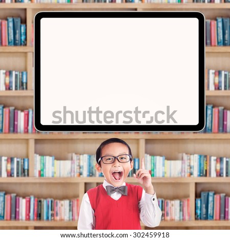 Joyful male primary school student pointing at a blank whiteboard in the library