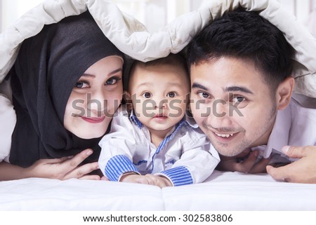 Portrait of attractive muslim family smiling on the camera with a sweet baby, shot below a blanket