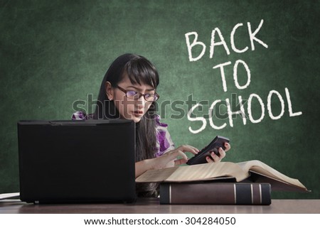 Female high school student back to school and using laptop, books, calculator for studying in the class