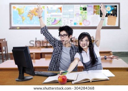 Portrait of two cheerful high school student studying in the classroom and raise hands together