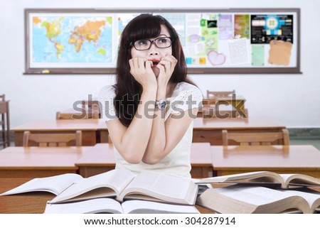 Portrait of female high school student sitting and studying in the classroom with scared expression