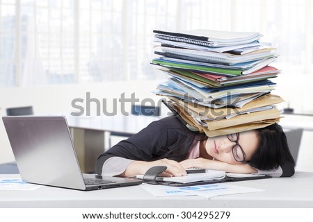 Frustrated businesswoman sleeping in the office with paperwork on head and laptop on the table