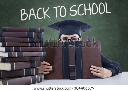 Female high school student back to school and look at the camera while holding book and wearing mortarboard