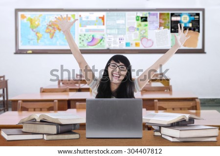 Happy female high school student studying in the classroom with laptop and raise hands