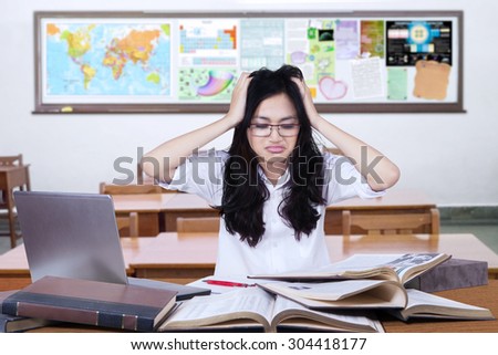Portrait of female high school student studying in the classroom and looks confused, scratching her hair and head