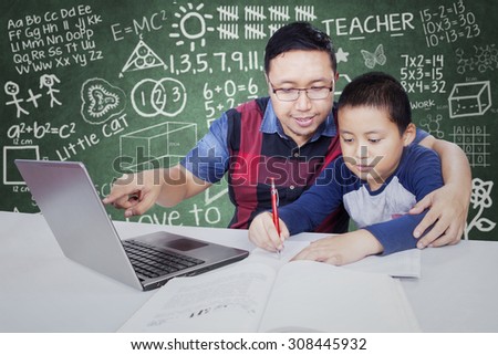 Young teacher pointing at laptop in the classroom while guiding his male student to study