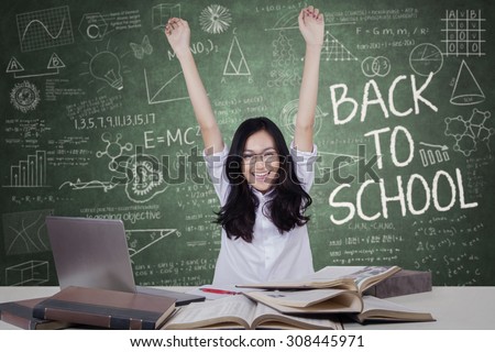 Portrait of female student celebrate back to school in the classroom while raising hands