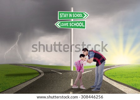 Portrait of young father kissing his daughter on the road with road sign to stay or leave school