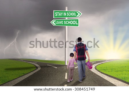 Rear view of father and his daughter walking on the road with road sign to stay or leave school