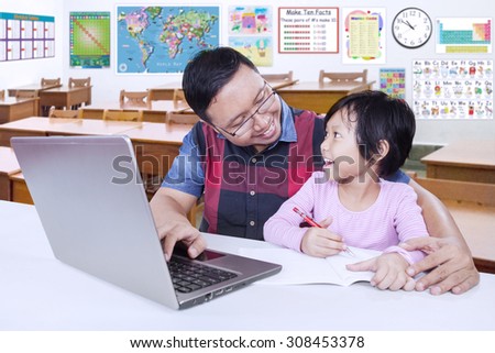 Portrait of male teacher talking with female elementary school student in the classroom while helping her to study