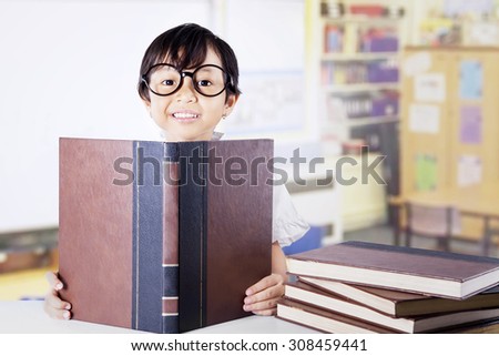 Lovely female student sitting in the class while wearing glasses and reading textbooks