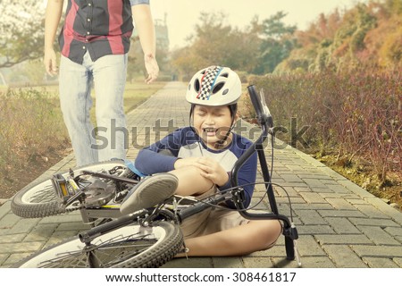 Little boy wearing helmet and crying while holding his knee after accident with his bike