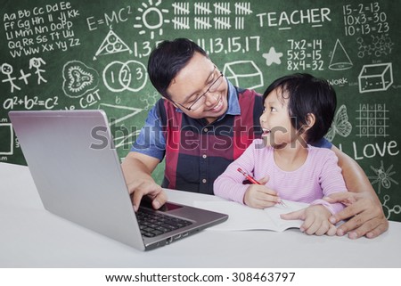 Portrait of male tutor speaking with his student in the classroom while helping her for studying with a book and laptop