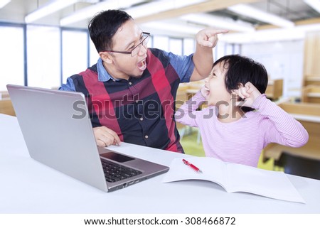 Portrait of little girl closing her ears and shouting on the teacher in the classroom