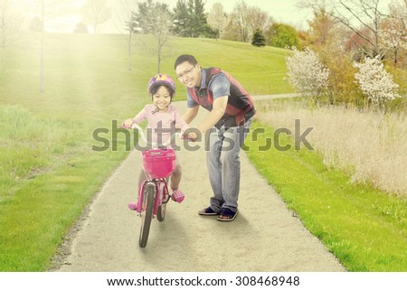 Portrait of young father helps his daughter riding a bicycle on the park