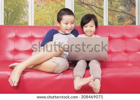 Portrait of little girl and her brother sitting on the sofa while using laptop to watch movie at home