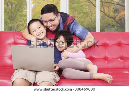 Two cheerful children using laptop computer for watching movie with their father at home