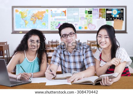 Group of three mixed race student studying together in the class and smiling at the camera