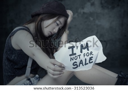 Portrait of frustrated girl victim of human trafficking, sitting alone with a paper